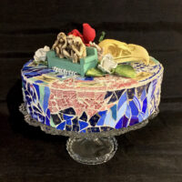 N. D. ceramic and glass with Capodimonte Rose, Bald Eagle Skull resin replica, carved three wise monkeys and vintage bench on crystal glass cake plate. 12 inch diameter, 3 1/4 inches tall, 7 1/4 inches with cake plate.